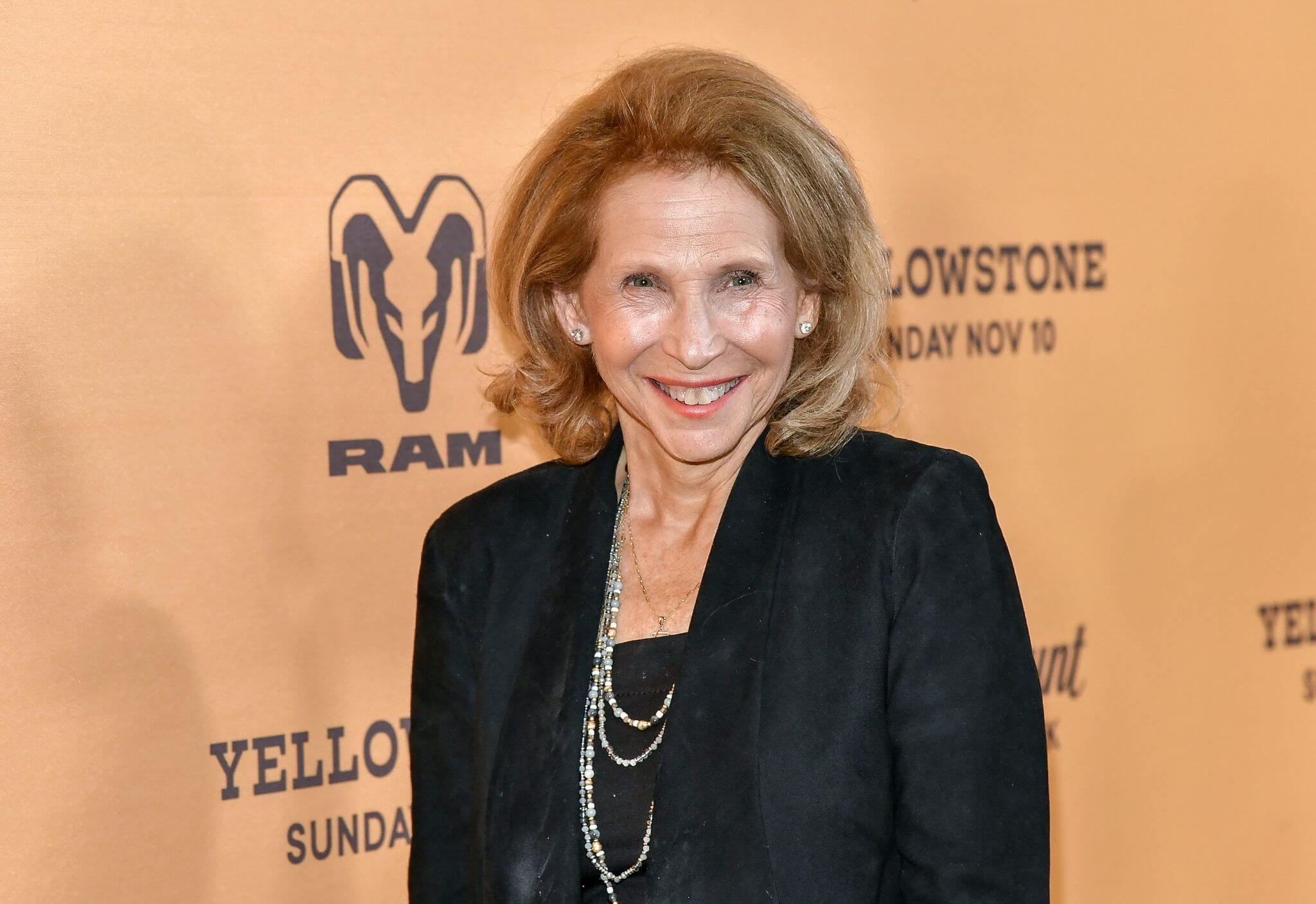 An older white woman in black suit smiles at the camera