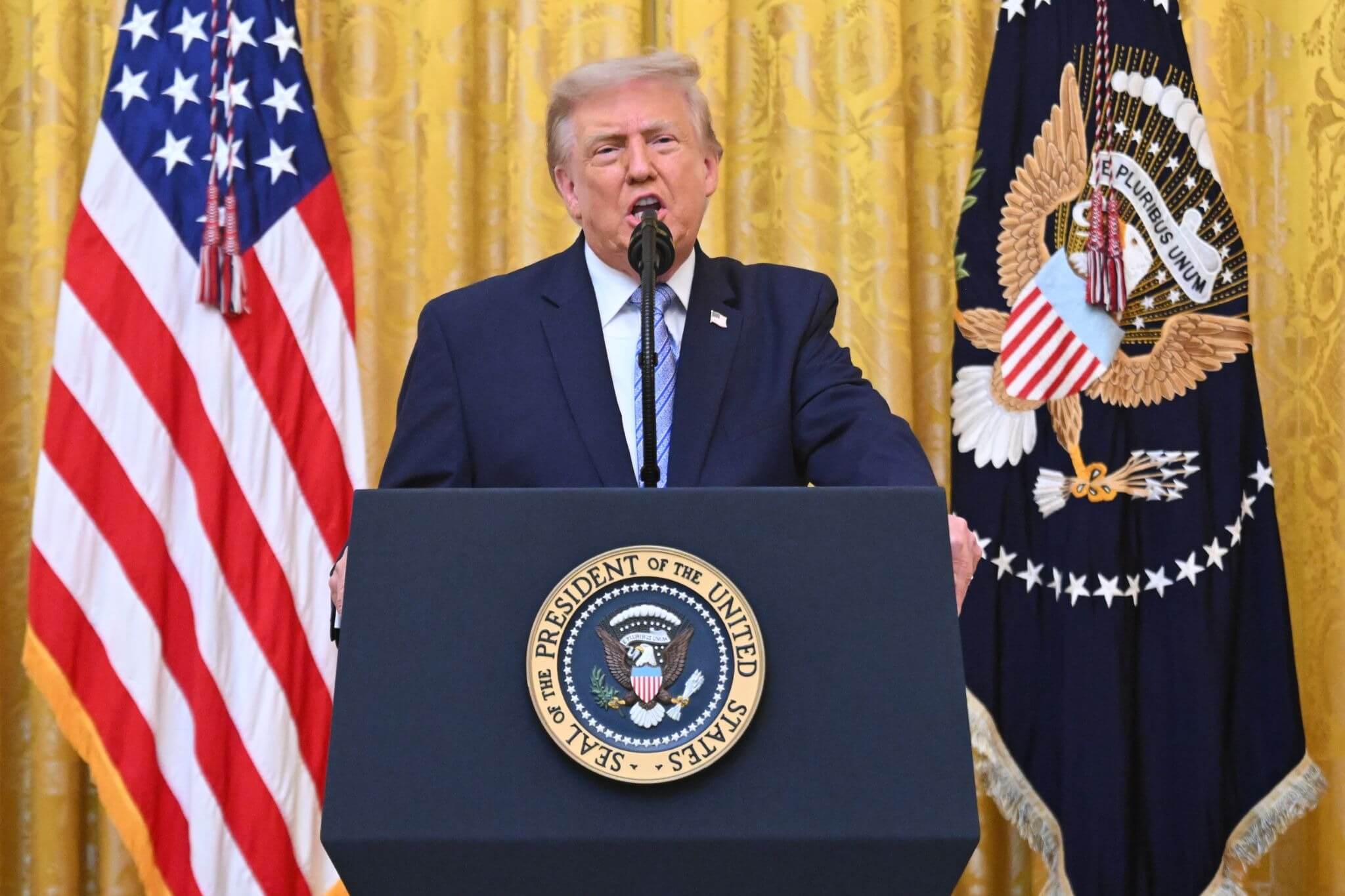 An older man in a suit standing at a podium speaking