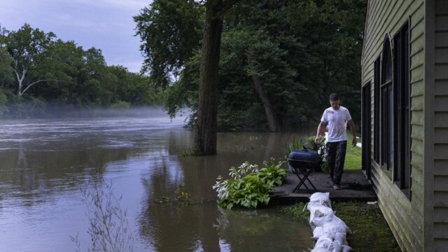 Man walking in flooded area behind a house.