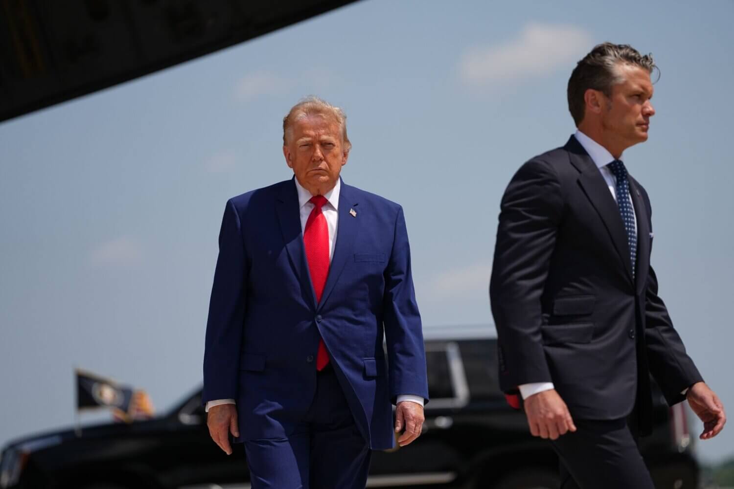 Two older men in suits leaving a vehicle and walking toward the camera