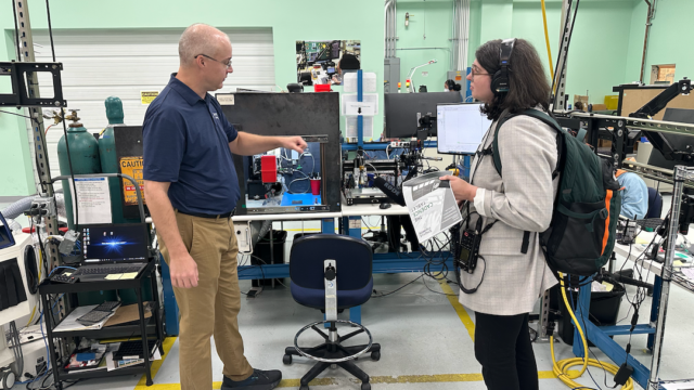 Female radio reporter interviews a man in an engineering factory.